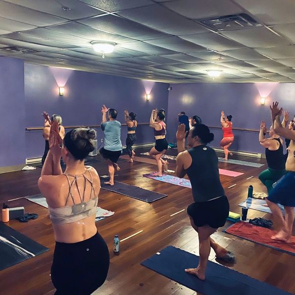 A full class of athletes practicing Eagle Pose (Garudasana) to improve balance, joint stability, and focus at The Hot Yoga Spot.